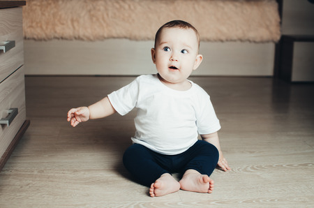 little baby girl sitting on the floor in an interesting and funny pose, happy