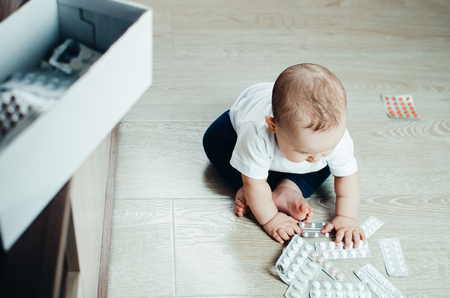 baby, girl sitting on the floor in the hands of pills, pulled out of the box or out of the closetの写真素材
