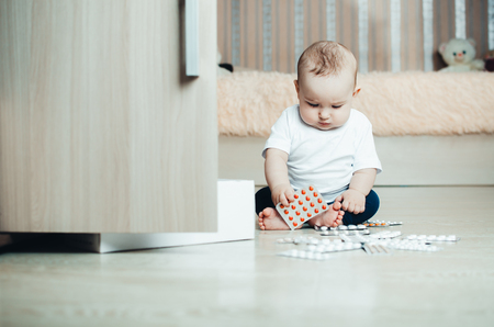 baby, girl sitting on the floor in the hands of pills, pulled out of the box or out of the closetの写真素材