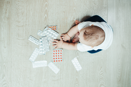 baby, girl sitting on the floor in the hands of pills, pulled out of the box or out of the closetの写真素材