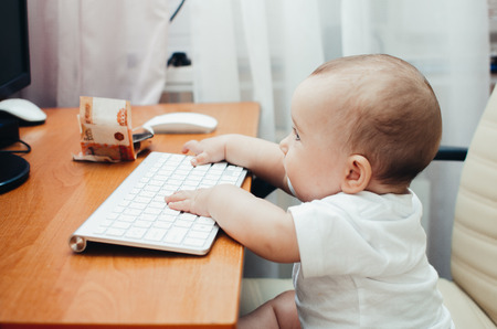 cute little baby girl typing on keyboard sitting at computerの写真素材