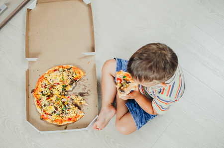 charming boy sitting on the floor eating pizza top viewの写真素材