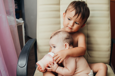 brother feeding little sister with milk or cereal with a bottleの写真素材