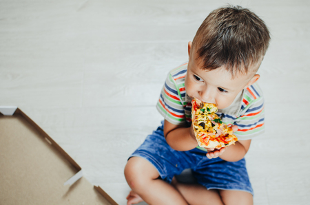 the child sits on the floor and eats pizza very appetizing and greedy, in shorts and a t-shirtの写真素材