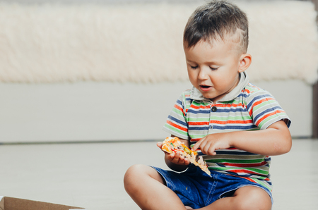 the child sits on the floor and eats pizza very appetizing and greedy, in shorts and a t-shirtの写真素材
