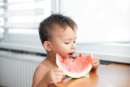 Cute little boy eating watermelon in the kitchen, very cuteの写真素材