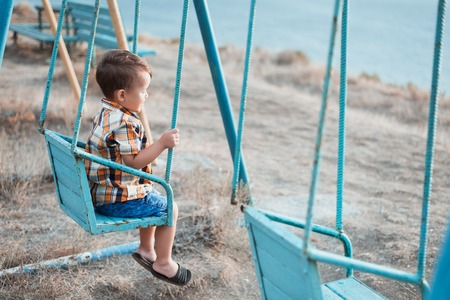 Baby on swing swinging one near the sea, in shirt and denim shorts