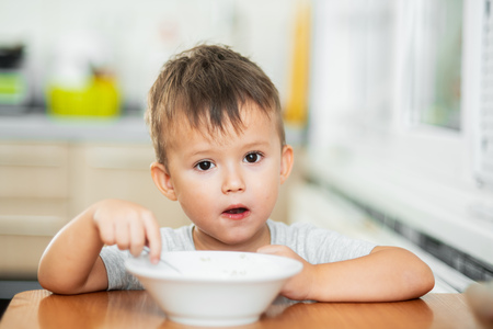 a charming child in a t-shirt in the kitchen eats oatmeal very greedilyの写真素材