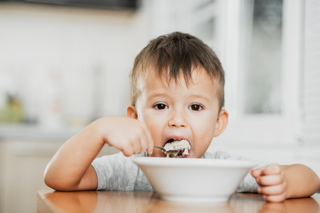 a charming child in a t-shirt in the kitchen eats oatmeal very greedilyの写真素材