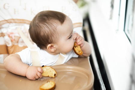 A child in a high chair eating a cracker with raisinsの写真素材