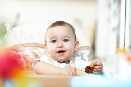 A child in a high chair eating a cracker with raisins