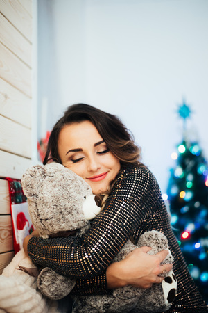 Beautiful girl with a bear in her hands on the background of lights and Christmas treeの写真素材