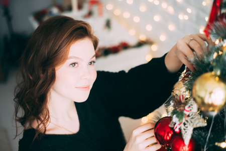 a beautiful girl in a sweater decorates a Christmas treeの写真素材