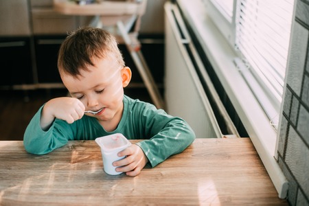 child eating yogurt in the kitchen in a green jacket, daylightの写真素材