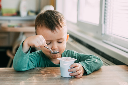 child eating yogurt in the kitchen in a green jacket, daylightの写真素材