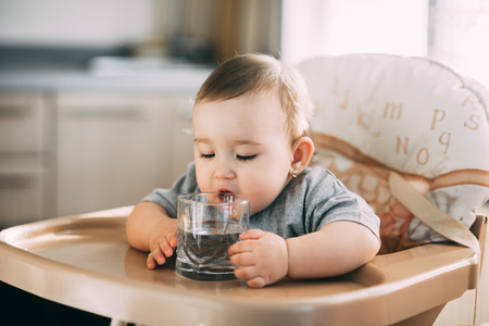 A child on a high chair drinking water from a glassの写真素材