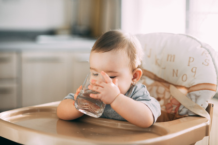 A child on a high chair drinking water from a glassの写真素材