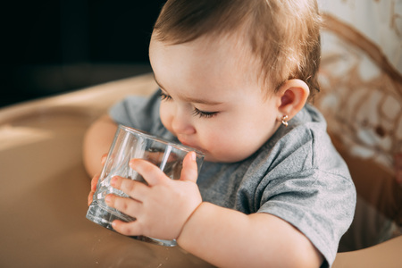 A child on a high chair drinking water from a glass