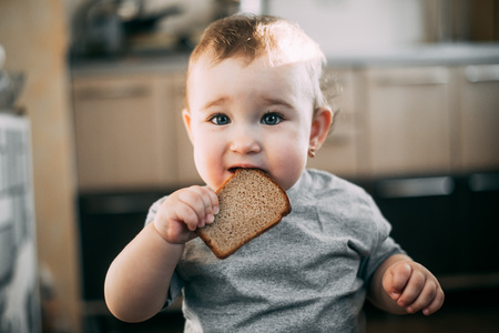 baby girl in the kitchen eating grey bread is very appetizing