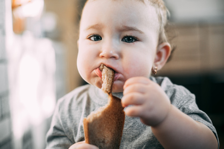 baby girl in the kitchen eating grey bread is very appetizing