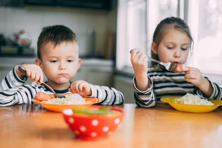 Children eat pasta and sausage in the kitchenの写真素材
