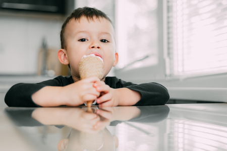 A child in a dark-blue t-shirt in the bright kitchen eating a waffle ice cream cone in the summer houseの写真素材
