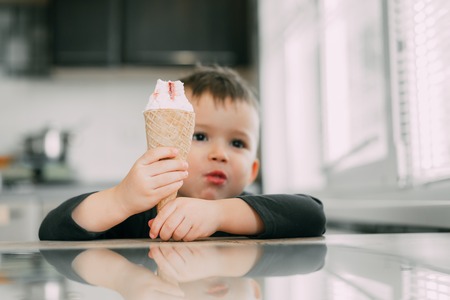 A child in a dark-blue t-shirt in the bright kitchen eating a waffle ice cream cone in the summer houseの写真素材