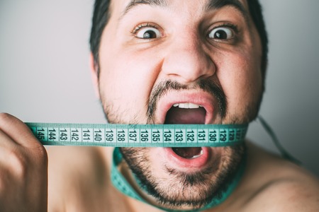Portrait of bearded frustrated fat man with green measuring tape around his mouth, healthy eating...