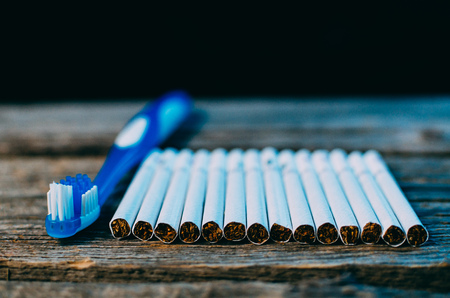 toothbrush and cigarettes on wooden table on black background