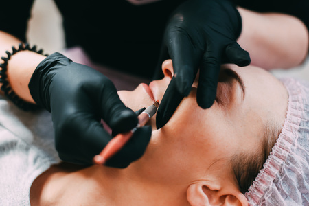 Permanent make-up for red Lips of beautiful woman in beauty salon. Closeup beautician doing tattooing Lips.の写真素材