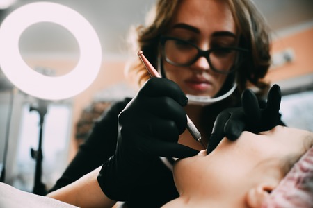 Permanent make-up for red Lips of beautiful woman in beauty salon. Closeup beautician doing tattooing Lips.の写真素材