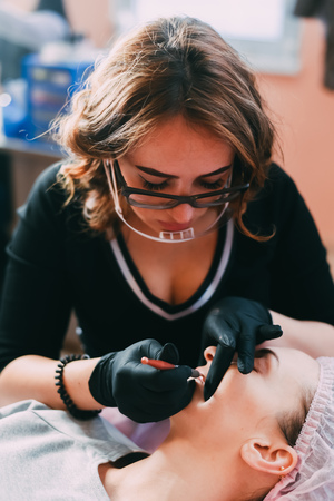 Permanent make-up for red Lips of beautiful woman in beauty salon. Closeup beautician doing tattooing Lips.の写真素材