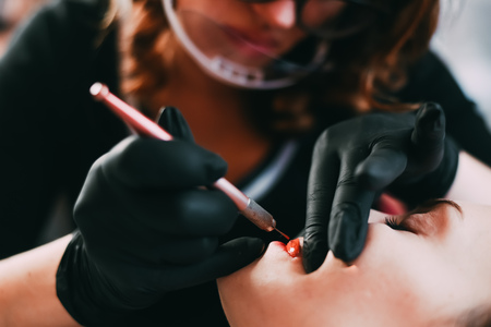 Permanent make-up for red Lips of beautiful woman in beauty salon. Closeup beautician doing tattooing Lips.の写真素材