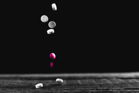 Pink and white pills fly sypyatsya on a wooden table on a black backgroundの写真素材