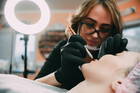 Permanent make-up for red Lips of beautiful woman in beauty salon. Closeup beautician doing tattooing Lips.の写真素材