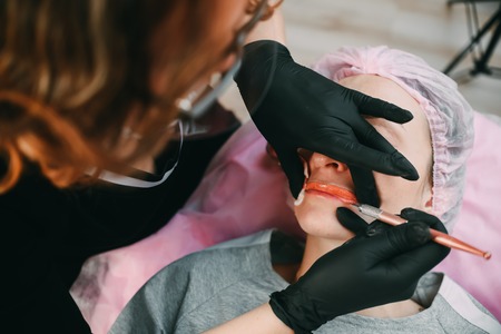 Permanent make-up for red Lips of beautiful woman in beauty salon. Closeup beautician doing tattooing Lips.の写真素材