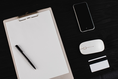 On the black wooden table lie phone credit card white, a sheet of paper in a folder, a mouse and a penの写真素材