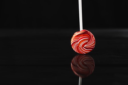red, round colored Lollipop on black background, with reflection