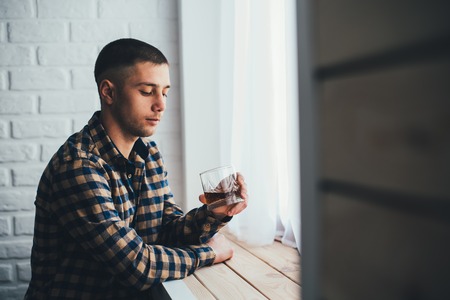 Young businessman with a glass of whiskey and a white brick wallの写真素材