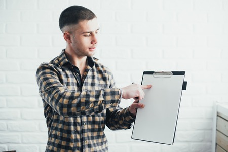 A man in a plaid shirt shows on the clipboard, on the background of the Kerp wallの写真素材