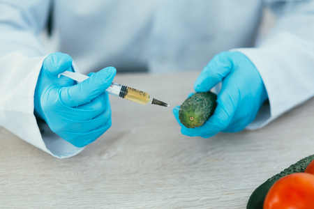 lab technician in lab coat and gloves colitis nitrates and GMO in cucumber on white background in...