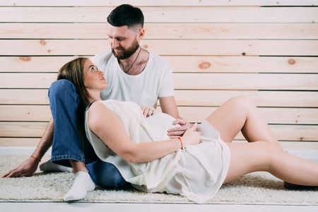 Young pregnant woman with husband sitting on floor on wooden backgroundの写真素材