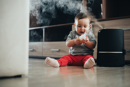 Little baby looks at the humidifier. Moisture in the house conceptの写真素材