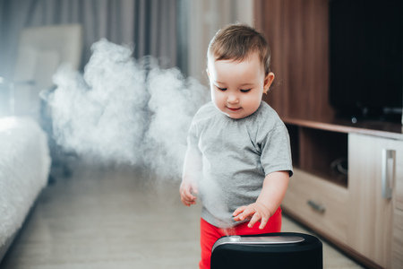 Little baby looks at the humidifier. Moisture in the house conceptの写真素材