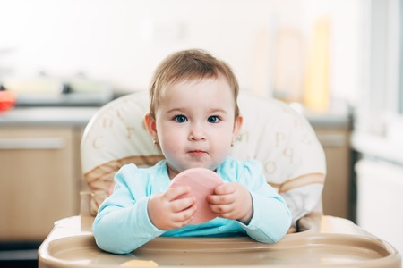a little girl in a high chair with a piece of boiled sausage in her handsの写真素材