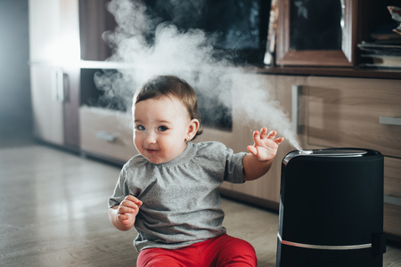 Little baby looks at the humidifier. Moisture in the house conceptの写真素材