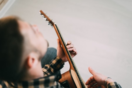 Handsome mature man in casual clothes is smiling while playing guitar at home