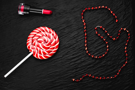 red round Lollipop on black background with texture near lipstick and beads of red colorの写真素材