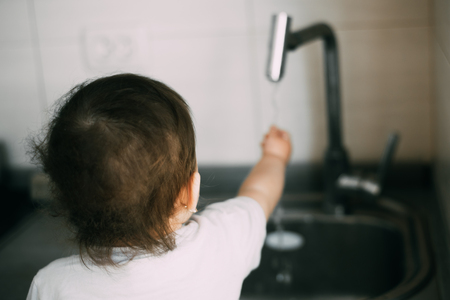 Little girl washes her hands in the kitchen by herselfの写真素材
