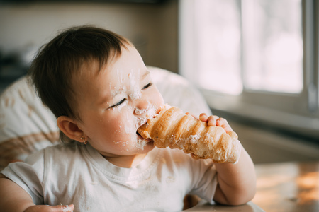 baby in the kitchen eagerly eating the delicious cream horns, filled with a vanilla creamの写真素材
